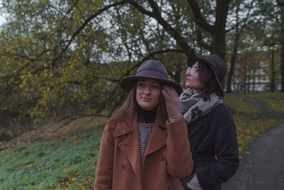 Two young women standing by tree against plants