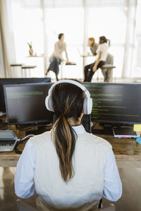 Rear view of male programmer working on computer at desk in office