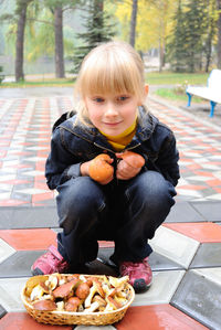 Portrait of girl crouching by mushrooms in yard