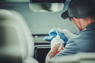 Rear view of cleaner cleaning while sitting in car