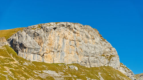 Low angle view of rocky mountain against clear blue sky