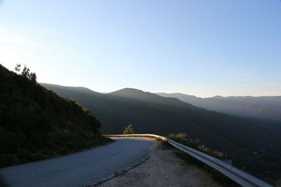 Road leading towards mountains against clear sky