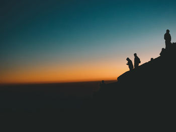 Silhouette people standing on land against sky during sunset