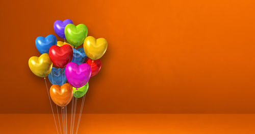 Close-up of multi colored balloons on table against orange background