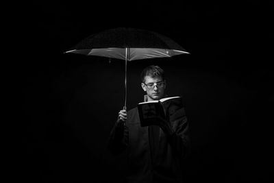 Portrait of young man standing against black background