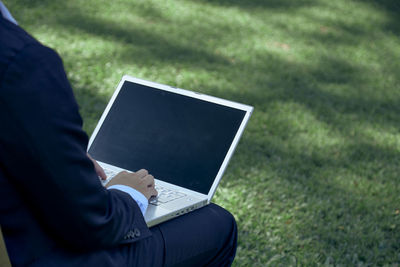 Midsection of man using mobile phone in grass