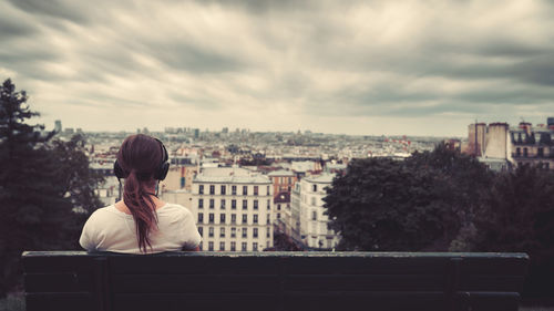 Rear view of woman sitting on bench against sky during sunset