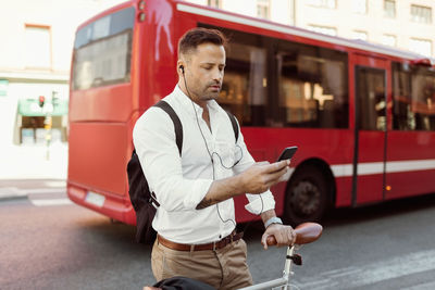 Businessman using smart phone while standing with bicycle on city street