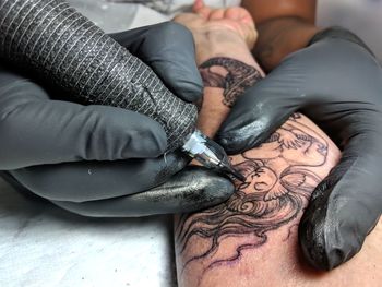 Cropped image of artist making tattoo on woman hand