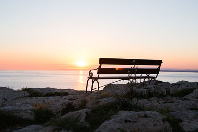 Lifeguard hut on rocks at beach against sky during sunset