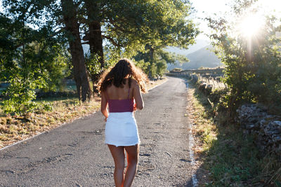 Rear view of girl walking on road amidst trees