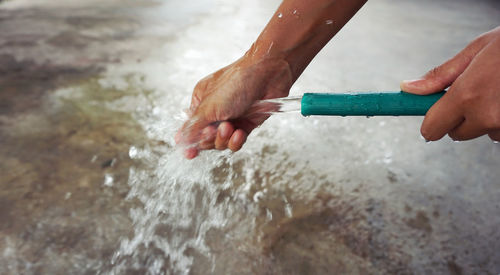 Cropped image of person washing hands with garden hose on footpath