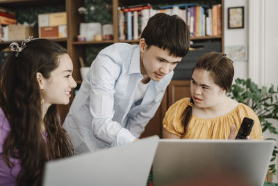 Teenage boy explaining down syndrome sister over laptop at home