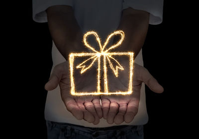 Midsection of man holding illuminated lighting equipment against black background