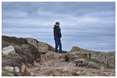 Rear view of man standing on cliff against sky