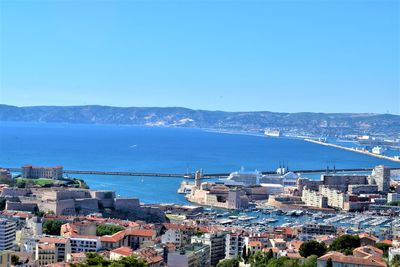 High angle view of townscape by sea against clear blue sky