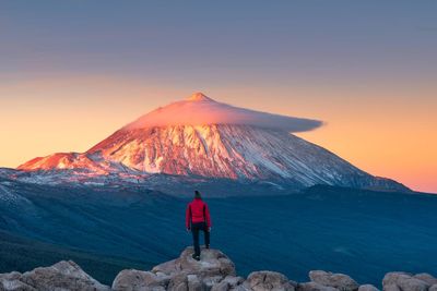 Rear view of man standing on mountain against sky during sunset