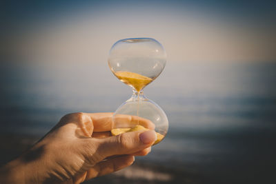 Midsection of person holding glass against sea