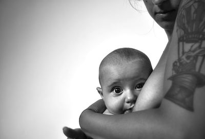 Midsection of woman breastfeeding baby against wall