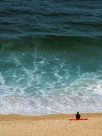 High angle view of man sitting on surfboard at beach