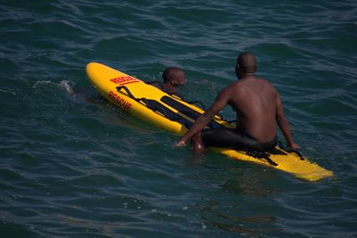 Shirtless man sitting on inflatable raft by friend in sea