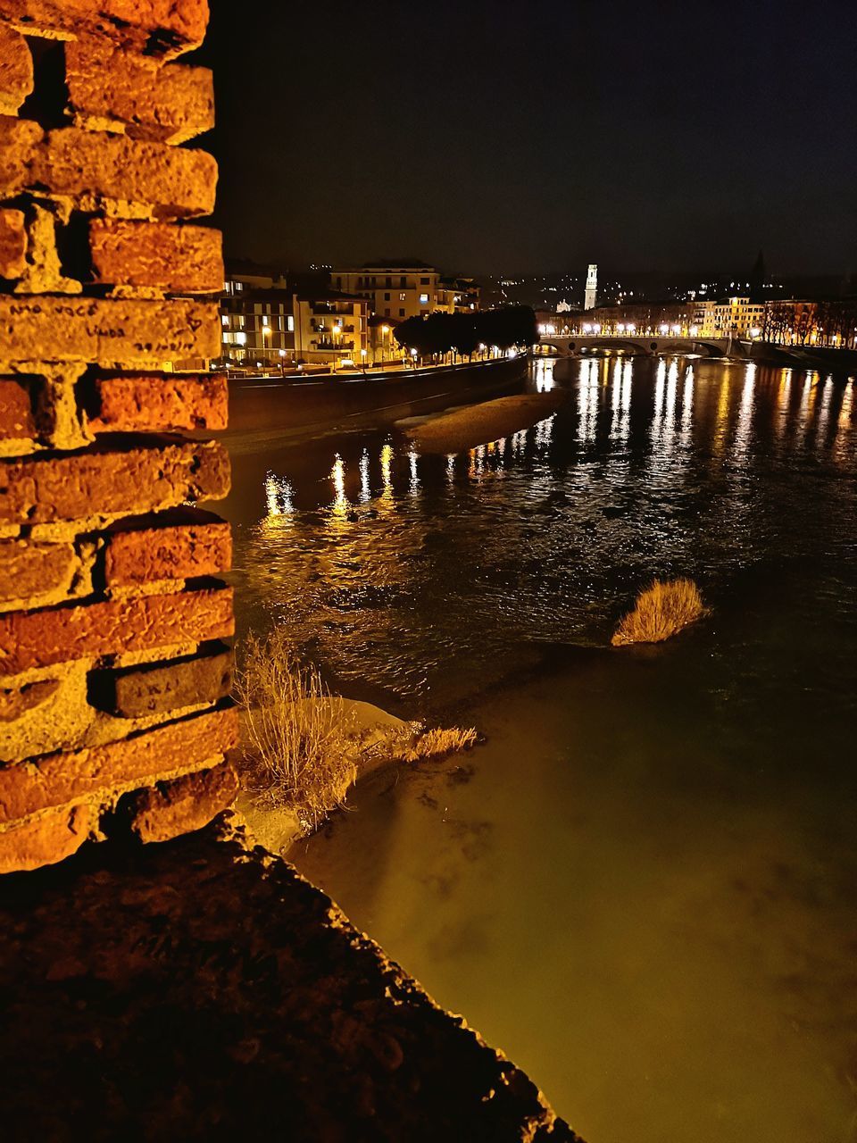 ILLUMINATED BUILDINGS BY RIVER AGAINST SKY IN CITY AT NIGHT