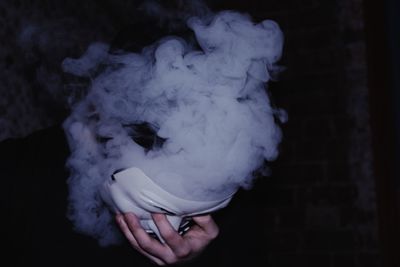 Cropped image of person holding mask emitting smoke