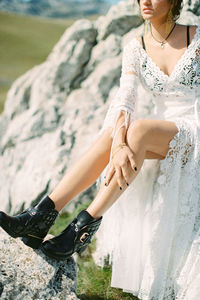 Low section of bride sitting on rock outdoors
