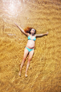 Pregnant woman wearing bikini lying on seashore at beach