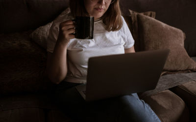 Midsection of woman using mobile phone while sitting on sofa at home