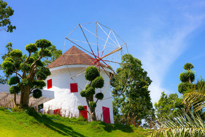 Traditional windmill by tree and building against sky