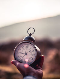 Close-up of hand holding clock against blurred background