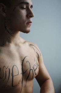 Shirtless young man with tattoo standing against wall