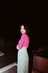 Portrait of young woman standing against black background