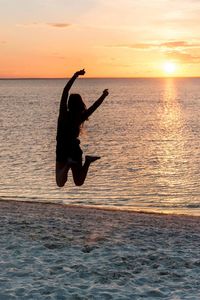 Silhouette man jumping in sea against sunset sky