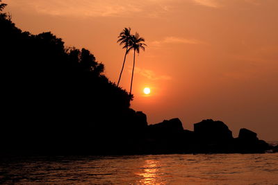 Silhouette mountains and trees by sea against sky during sunset