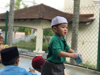 Boy looking away while standing against built structure