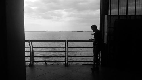 Silhouette man standing by railing against sea