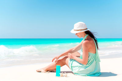 Woman sitting on beach by sea against sky