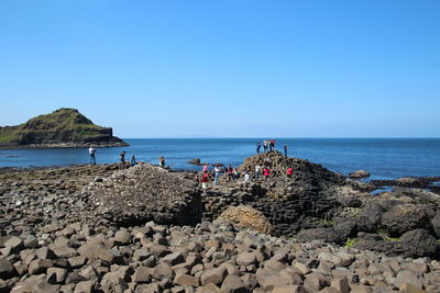People on rocks at beach against clear blue sky