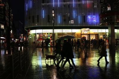 People walking on illuminated street amidst buildings in city at night