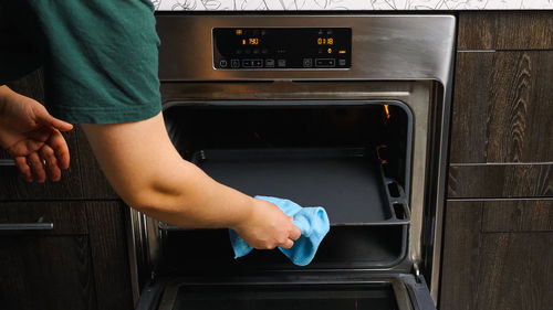 A woman's hand opens the oven door and pulls out a tray. preparing to bake a meal