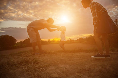 Side view of man standing on field against sky during sunset