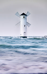 Lighthouse by sea against clear sky