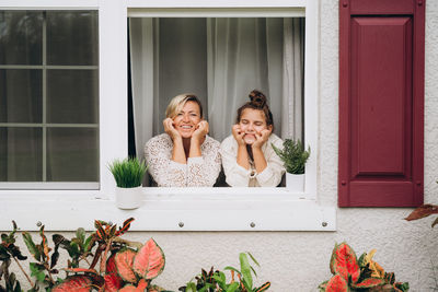 Smiling mother and daughter on window looking into the garden