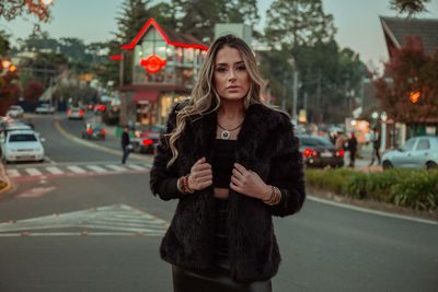 Portrait of young woman standing on road in city