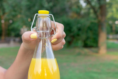 Beautiful woman is opening a bottle of fresh cold juice on the bench in the park in hot summer day