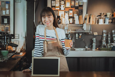 Close-up portrait of young woman holding coffee drink while standing in cafe