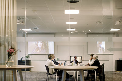 Business people discussing in global conference meeting seen through glass wall at office