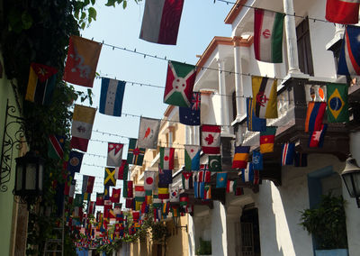 Low angle view of flags hanging amidst buildings against sky